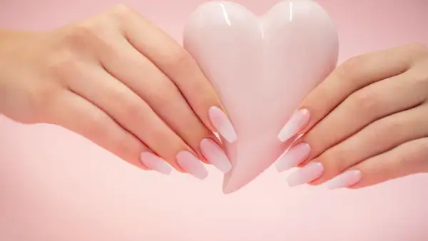 Mains délicates tenant un cœur rose pâle, manucure baby boomer couleur pastel.