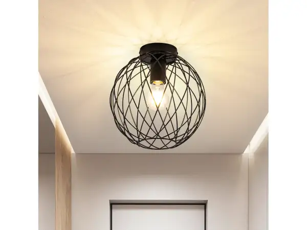 Nowoczesna lampa sufitowa z czarną, drucianą kulą i widoczną żarówką, tworząca ciekawe cienie na suficie.