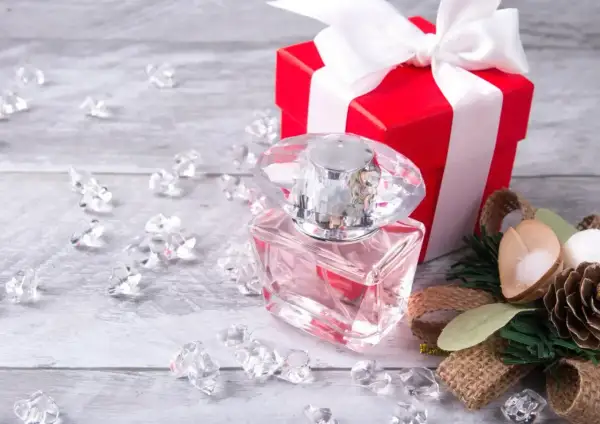 Eleganckie perfumy w szklanej butelce, czerwone pudełko z kokardą i ozdoby. Idealny pomysł, jak zapakować perfumy na prezent.