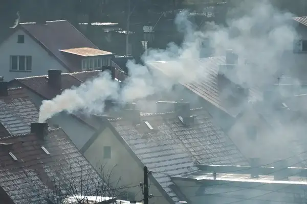 Dym wydobywający się z kominów domów na tle zachmurzonego nieba.