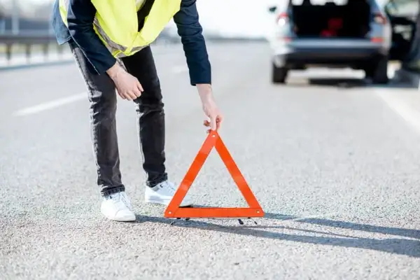 Hombre con chaleco reflectante coloca un triángulo de señalización tras una detención de coche en la carretera.
