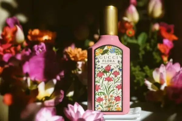 Różowa butelka Gucci Flora Gorgeous Gardenia otoczona bujnymi, kolorowymi kwiatami.