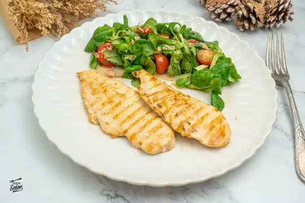 Dos pechugas de pollo a la plancha con marcas de parrilla, servidas con una ensalada fresca de hojas verdes y tomates.