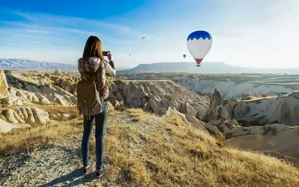 En kvinna med ryggsäck fotograferar den magiska vyn av luftballonger över Kappadokien, Turkiet.