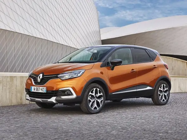 Pomarańczowy Renault Captur 2016 z czarnym dachem zaparkowany na brukowanej nawierzchni przed nowoczesnym budynkiem.
