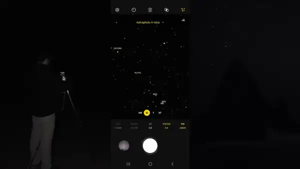 Mężczyzna robi zdjęcie nocnego nieba z Saturnem i Plutonem za pomocą telefonu Samsung. Tryb Astrophoto ustawiony na 4 minuty.