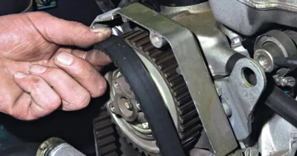 Dłoń mechanika sprawdza stan paska rozrządu, który jest kluczowym elementem silnika.
