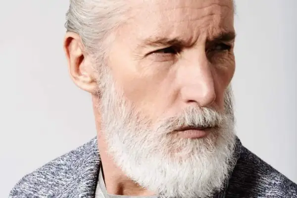 Un homme âgé au regard intense, arborant un modèle de barbe homme blanc et volumineux, avec des cheveux grisonnants coiffés en arrière.