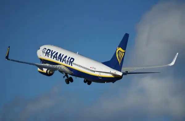 Samolot Ryanair wznoszący się na tle błękitnego nieba z chmurami.