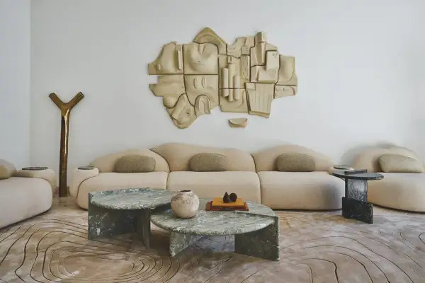 Salon moderne avec canapé beige, tables basses en marbre vert, sculpture murale abstraite et tapis aux motifs organiques. Un endroit parfait pour recevoir une lettre home.