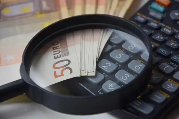 Lupe über 50-Euro-Scheinen auf einem Taschenrechner. Analyse von Betriebskosten und Umlageausfallwagnis.