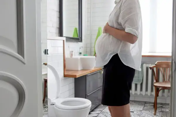 Schwangere Frau im Badezimmer, die sich wegen Durchfall in der Schwangerschaft unwohl fühlt.