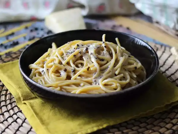 Miseczka spaghetti cacio e pepe, z kremowym sosem serowym i pieprzem, na żółtej serwetce.