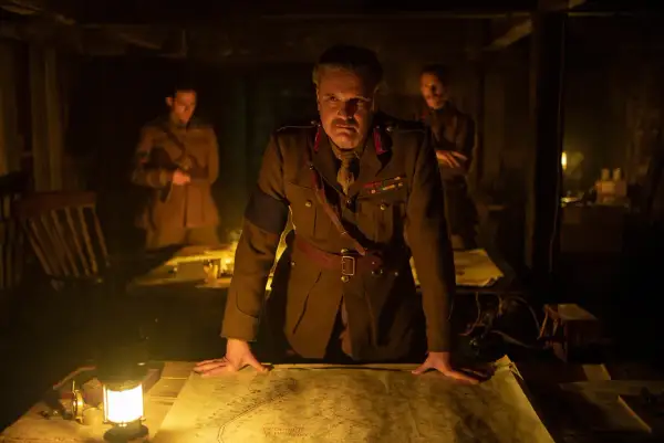 Ein General studiert im Schein einer Lampe eine Karte. Die besetzung von 1917 (film) zeigt ihn mit zwei Offizieren im Hintergrund.