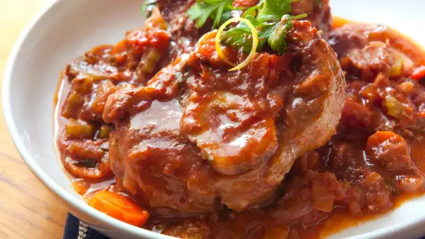 Herzhaftes Ossobuco Rezept in Tomatensoße mit Karotten und Petersilie, serviert in einer weißen Schüssel.
