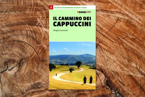 Copertina del libro "Il Cammino dei Cappuccini", con due frati che percorrono un sentiero tra colline verdi e dorate.