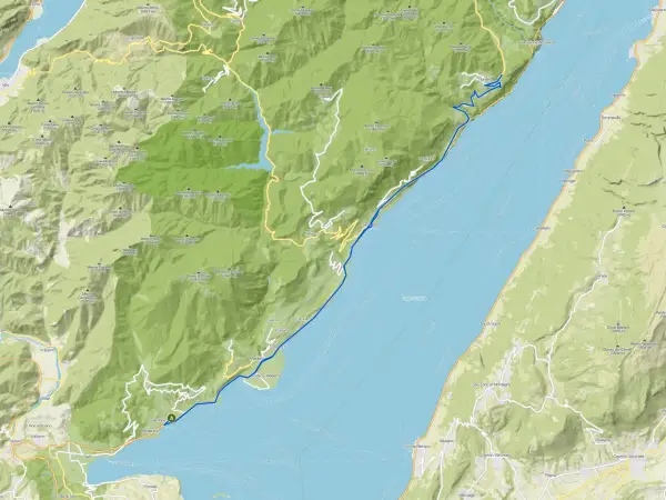 Il lungolago di Gardone Riviera si estende lungo il Lago di Garda, con montagne verdi che si affacciano sull'acqua.