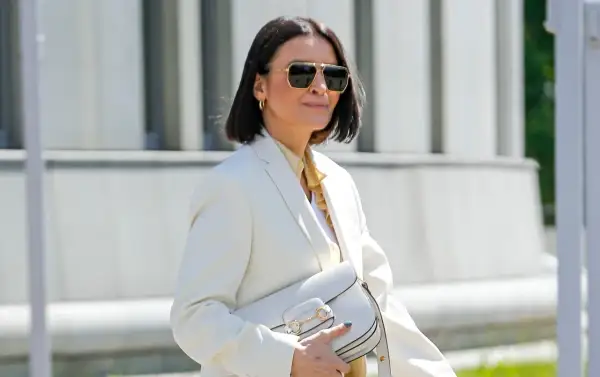 Elegancka kobieta po 50. w białej marynarce i okularach przeciwsłonecznych, z białą torebką. Stylowa moda po 50.