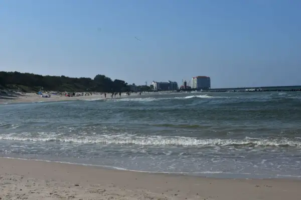 Słoneczny dzień nad Bałtykiem, plaża pełna ludzi, a w oddali widać miasto u ujścia Wieprzy.