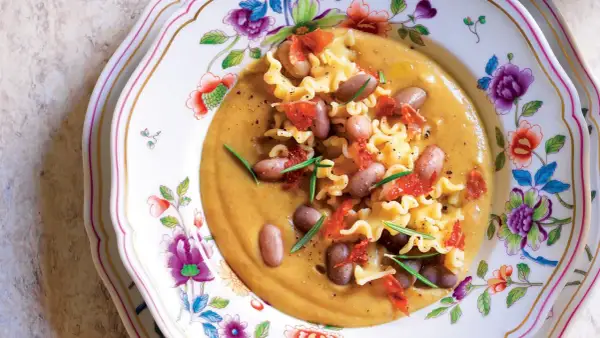 Pasta e Fagioli with ruffled pasta, beans, and crispy pancetta on a floral plate.