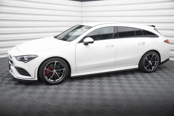 Biały Mercedes CLA shooting brake z czarnymi felgami i czerwonymi zaciskami hamulcowymi stoi na szarej, kratkowanej podłodze.
