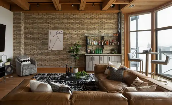 A rustic modern living room with exposed brick, wood beams, a leather sofa, and a home bar.