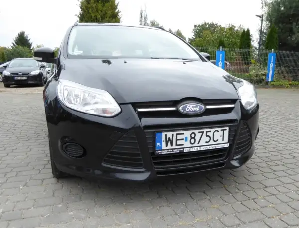 Czarny Ford Focus 2011 z tablicą WE 875CT zaparkowany na kostce brukowej.