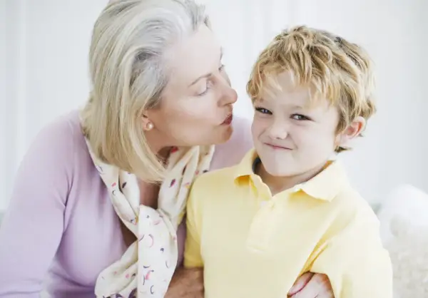 Una nonna bacia un bambino sorridente. Nonostante la tenerezza, i bambini non si baciano sempre, ma questo momento è speciale.