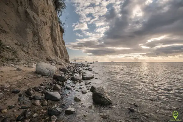 Klif w Gdyni, kamienista plaża i morze. W oddali widać statki. To jedna z pięknych gdynia atrakcji.