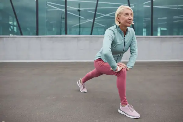 Donna bionda in abiti sportivi fa stretching, contrastando l'atonia muscolare con un affondo.