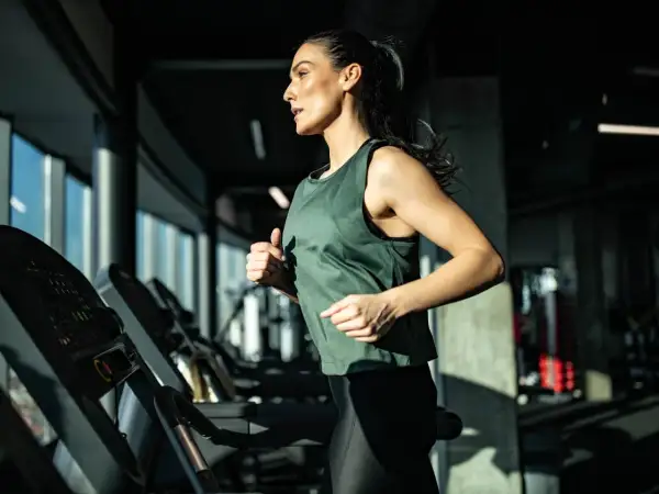 Eine Frau läuft auf einem Laufband im Fitnessstudio. Sie trainiert intensiv und zeigt, was ein Laufband für die Ausdauer bringt.