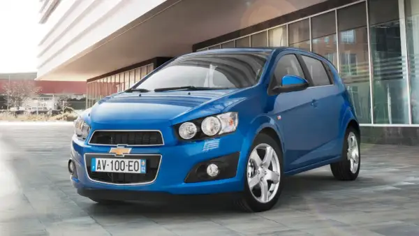 Błękitny Chevrolet Aveo stoi przed nowoczesnym budynkiem.