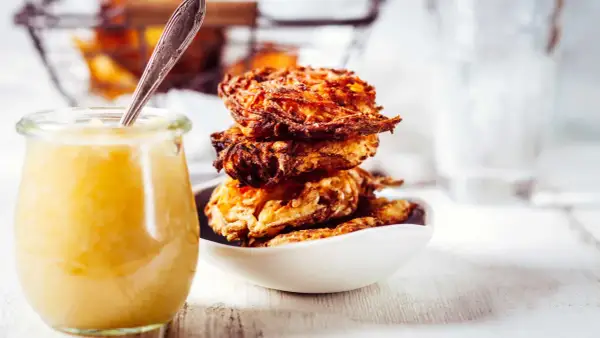 Goldbraune Kartoffelpuffer stapeln sich in einer Schüssel, daneben ein Glas Apfelmus. Ein perfektes Kartoffelpuffer Rezept für jeden Anlass.