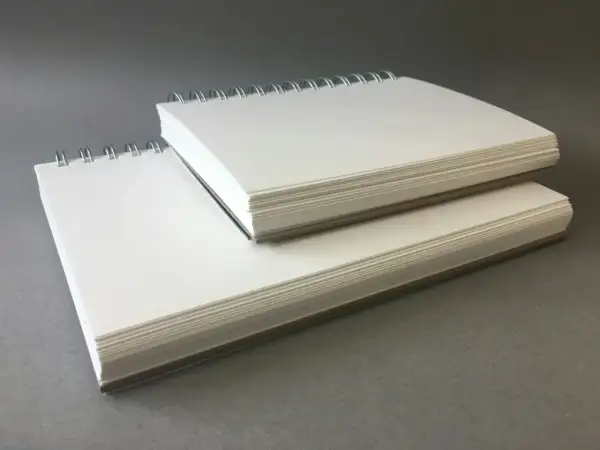 Deux carnets à spirales empilés, remplis de papier pour acrylique blanc épais, prêts pour la création artistique.