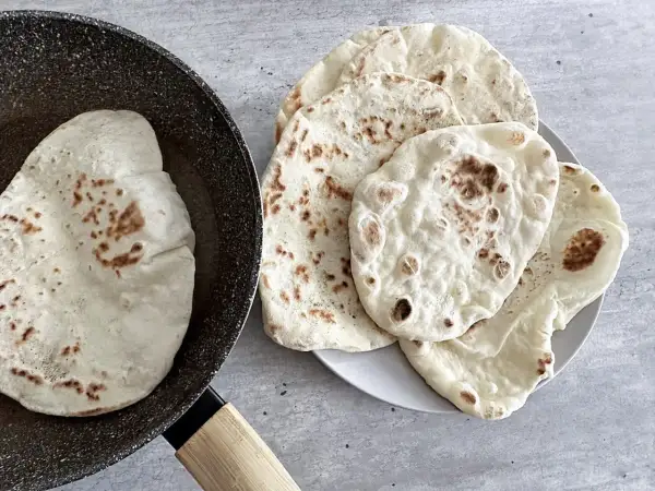 Chlebek naan przepis: świeżo usmażone placki na patelni i talerzu, gotowe do podania.