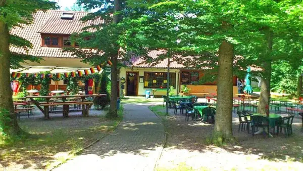 Idyllischer Biergarten mit vielen Tischen und Bänken unter Bäumen, dekoriert mit Deutschlandflaggen. Einladend für ein Treffen im Waldheim Backnang.