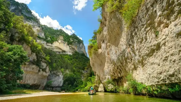 Wąwóz Gorges du Tarn, zielona rzeka i łódź z wioślarzami wśród skalnych ścian porośniętych bujną roślinnością.