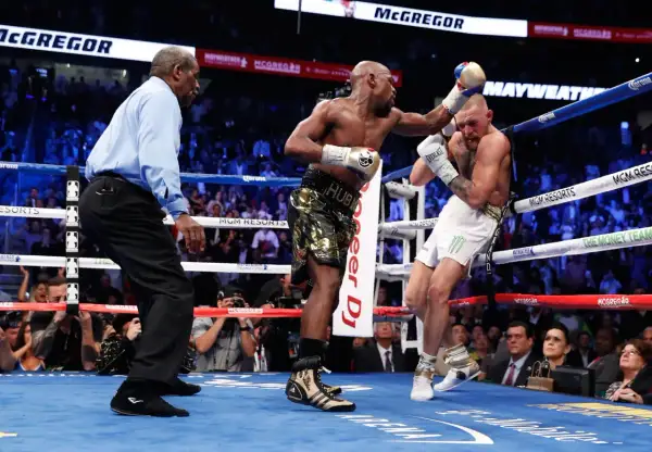 A referee watches as Floyd Mayweather Jr. lands a punch on Conor McGregor during their boxing match.