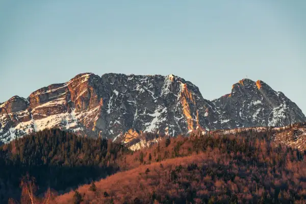 Ośnieżony Giewont w złotym świetle zachodzącego słońca, z lasem u podnóża. Zastanawiasz się, ile ma Giewont?