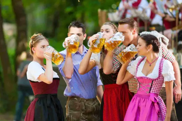Cinco amigos brindan con jarras de cerveza, celebrando cuando es Oktoberfest con trajes bávaros tradicionales.