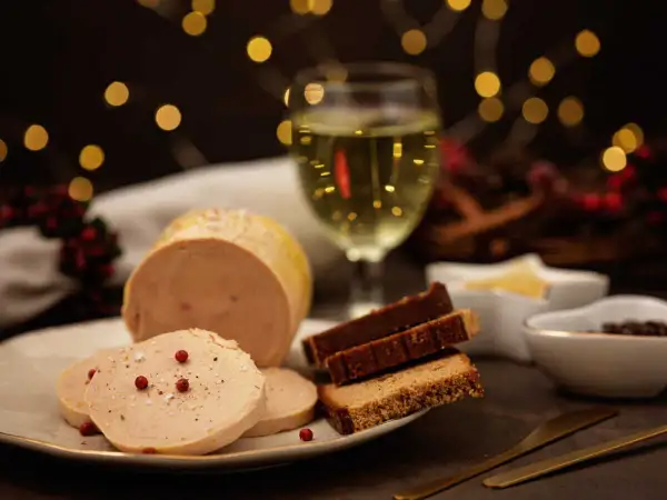 Un délicieux bloc de foie gras tranché, servi avec du pain d'épices et un verre de vin blanc, le tout dans une ambiance festive.