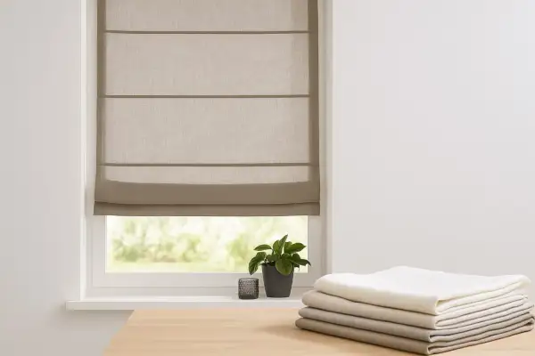 Ein beiger Raffrollo mit Vorhang kombinieren? Hier ist ein Beispiel: Ein schlichtes Raffrollo über einem Fenster, daneben ein Stapel Stoffe in verschiedenen Grautönen.