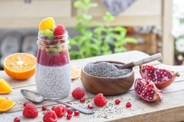 Un délice fruité : un pot de pudding de chia garni de fruits rouges, kiwi et orange, à côté d'une coupelle de graine de chia bienfait.