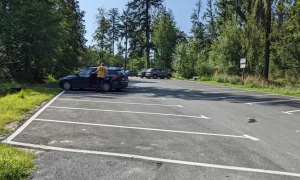 Parking przy szlaku na przełęcz Szarcula. Kilka samochodów na nowym, asfaltowym parkingu otoczonym lasem.