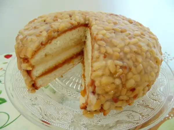 Tarta de piñones tradicional, con capas de bizcocho y mermelada, cubierta de piñones caramelizados. ¡Un dulce irresistible!