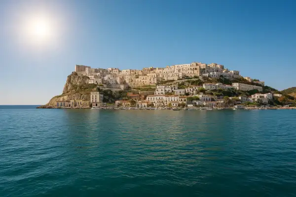La spiaggia La Cala di Peschici, con le sue case bianche aggrappate alla roccia, si specchia nel mare blu sotto un sole splendente.