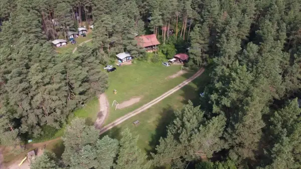 Malowniczy widok na stanicę wodną Zgon otoczoną lasem sosnowym. Widać domki, samochody i plac zabaw.