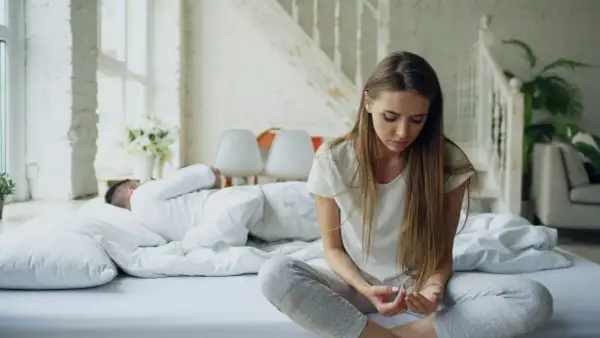 Een vrouw zit op bed, nadenkend na een ruzie. Haar partner slaapt ernaast. Ze is een hsp en voelt de spanning nog.