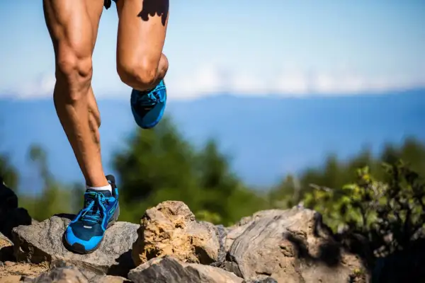 Nogi biegacza w niebieskich butach na kamienistym szlaku, przygotowującego się do ultramaratonu. Ile km? Tego nie wiemy, ale wysiłek jest widoczny.
