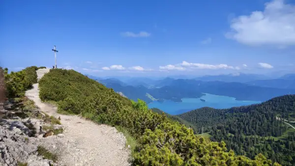 Gipfelkreuz nach einer Heimgarten Wanderung mit Blick auf einen türkisfarbenen See und Berge.